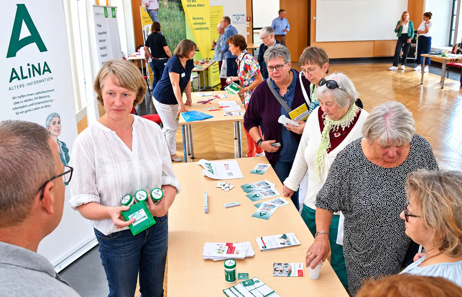 Mann spricht bei einer Veranstaltung vor Publikum; im Hintergrund ein Informationsstand.