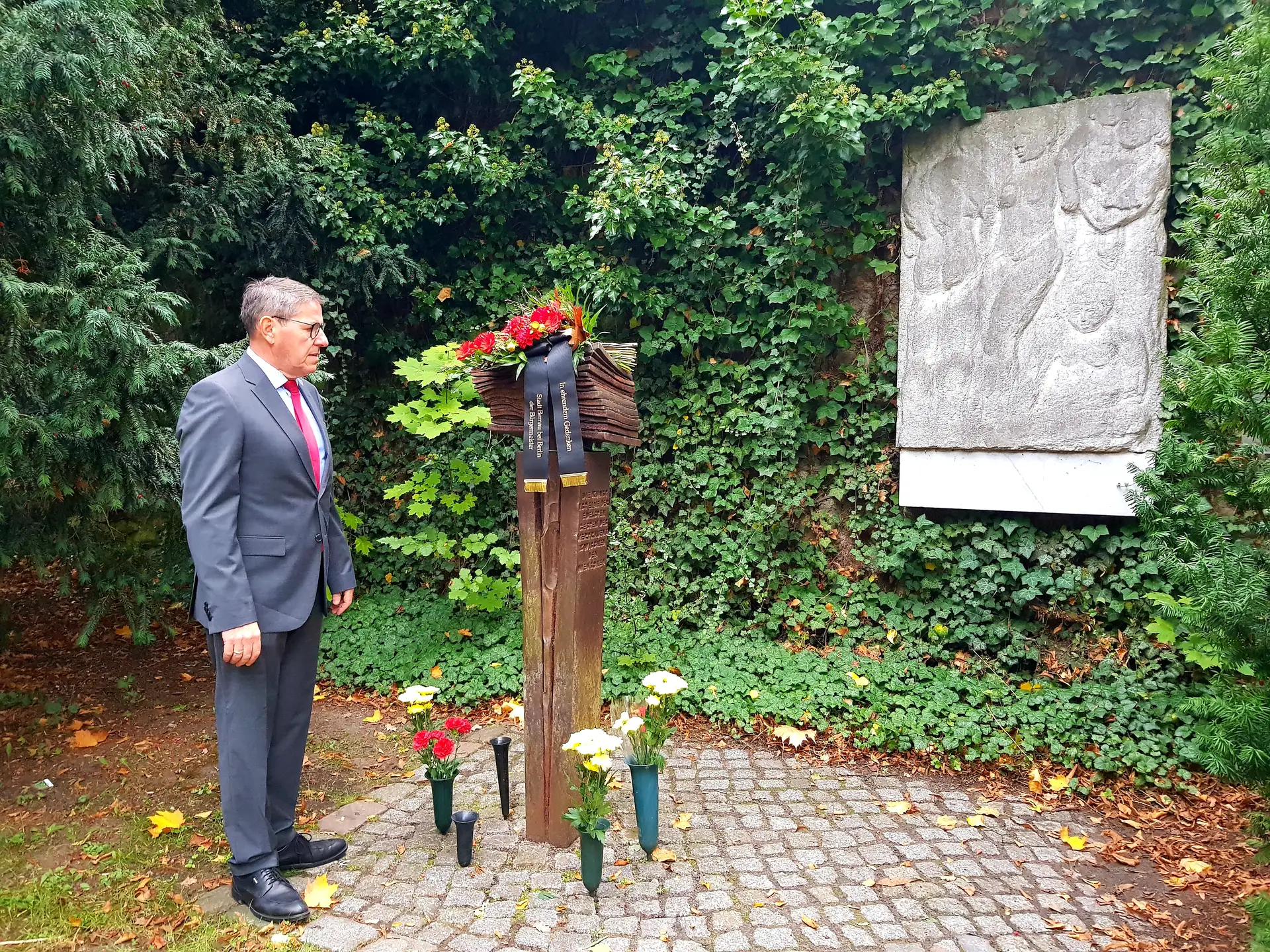 Bürgermeister André Stahl legt ein Blumengebinde am Konrad-Wolf-Denkmal im Stadtpark nieder.